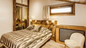 Ein gemütliches Schlafzimmer mit einem großen Bett, einem Holz-Kopfteil, einem Fenster mit Vorhängen, einem Sessel und einem Kamin.