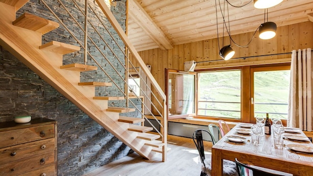 Eine Holztreppe mit einer Steinwand, ein Essbereich mit Tisch für vier Personen und ein Fenster mit Blick ins Freie.