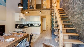 Ein modernes Interieur mit einer Holztreppe, einer Küche mit schwarz-weißen Fliesen und einem Essbereich mit Holztisch und -stühlen.