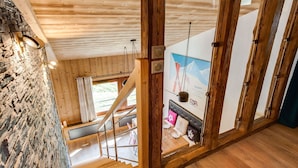 Ein Holzinnenraum mit einer Treppe zu einem Zimmer, das ein Bett, ein Fenster und ein Poster zeigt.