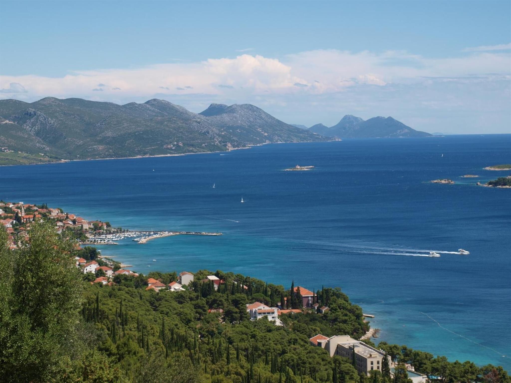 A coastal town with buildings along the shoreline, a clear view of the sea, and mountains in the background.