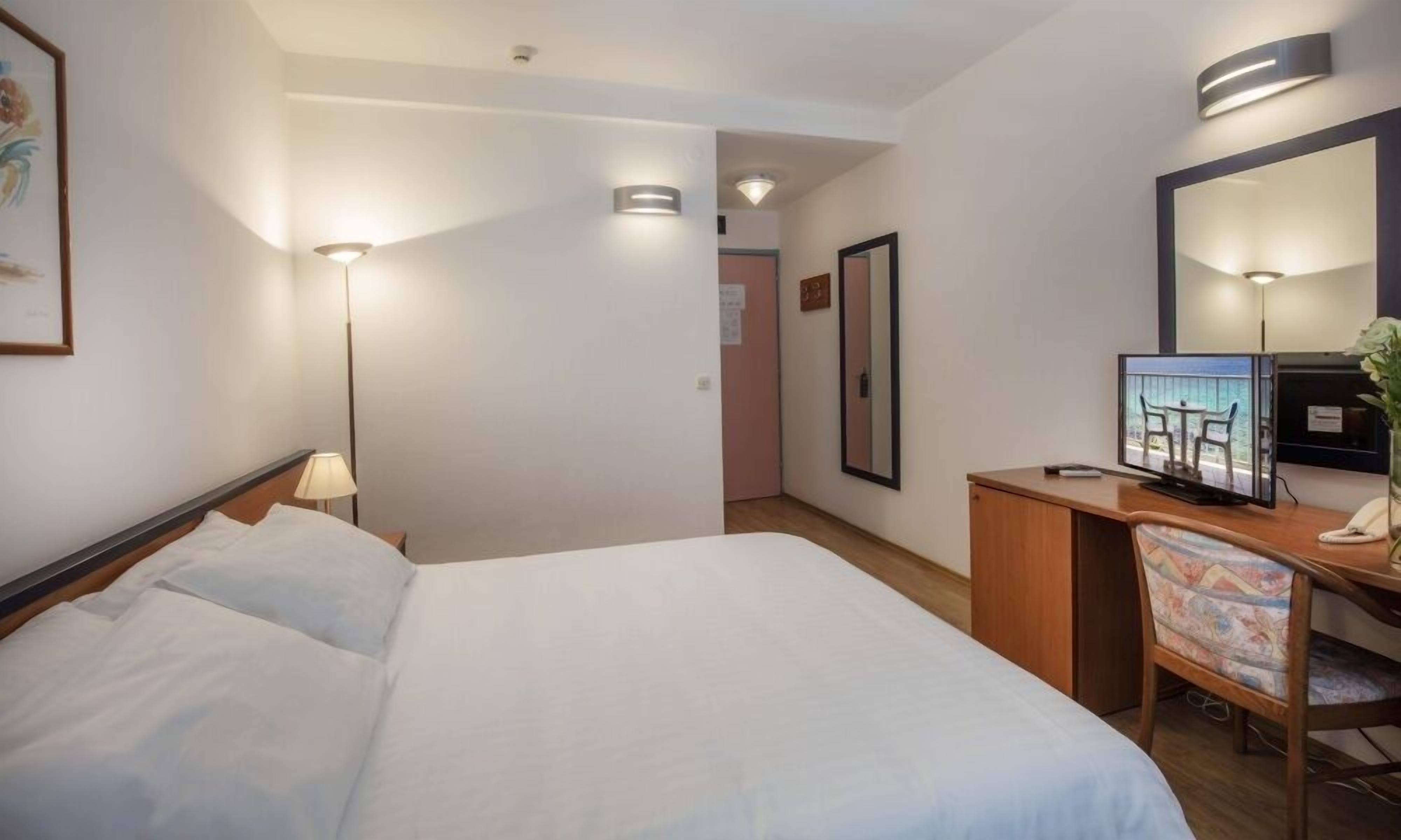 Een hotelkamer met een bed, bureau, stoel en een televisie waarop een mooi uitzicht te zien is.