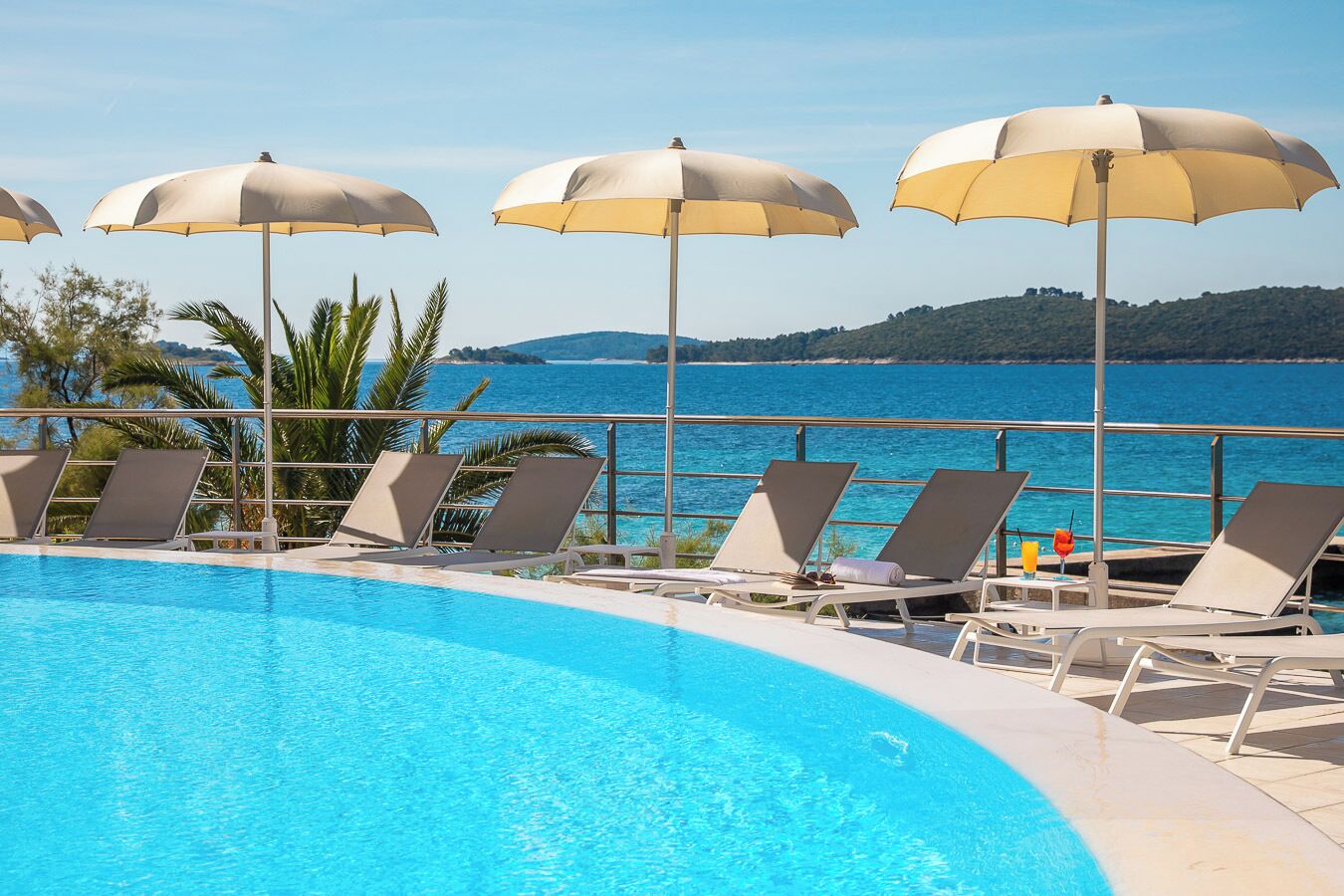 A poolside area with lounge chairs and umbrellas, overlooking a body of water and a distant landmass.