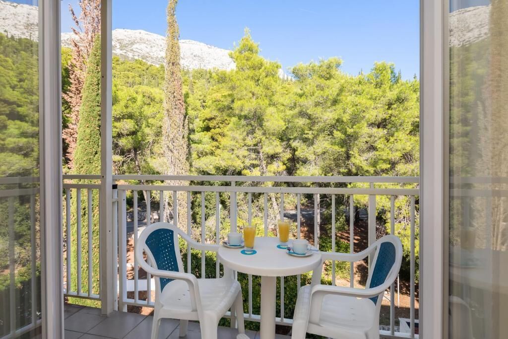 Un balcón con dos sillas blancas y una mesita, con vistas a un paisaje montañoso de abundante vegetación.