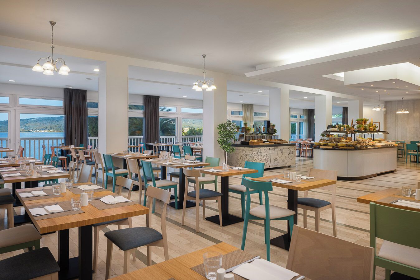 A spacious dining area with multiple tables and chairs, a central bar, and large windows offering a view of the outdoors.