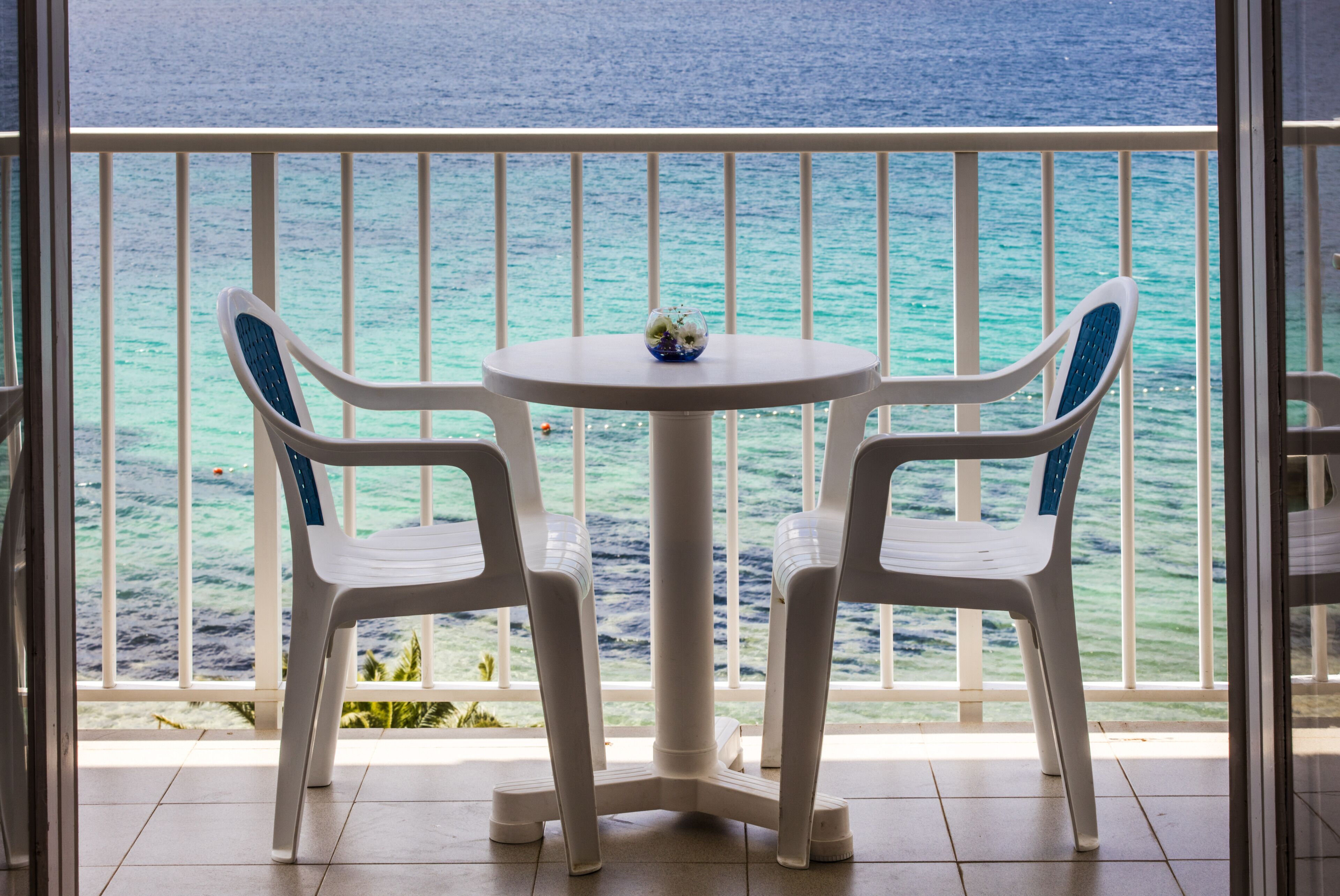 A balcony with two chairs and a table, overlooking a turquoise sea.