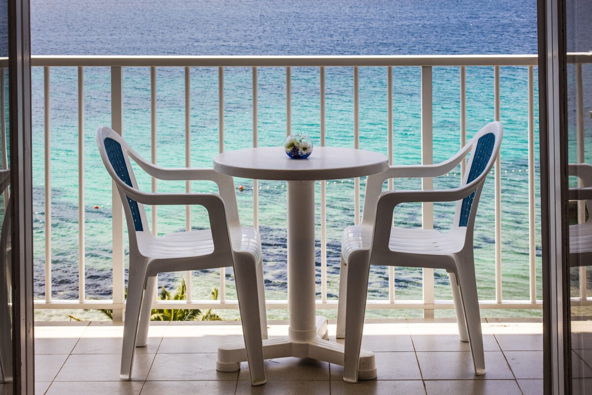 A balcony with two white plastic chairs and a small table, overlooking a turquoise sea.