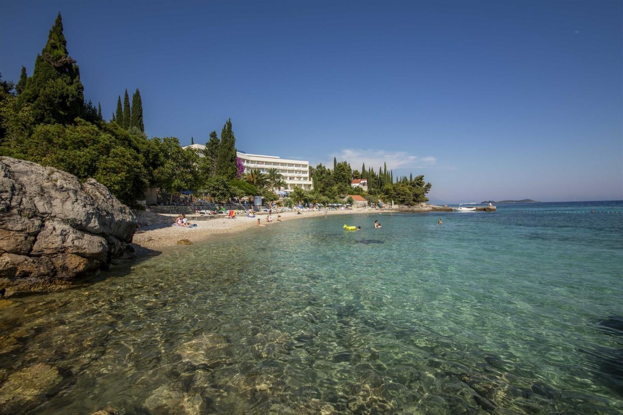 Una playa con agua cristalina, un litoral rocoso y un edificio de varios pisos.