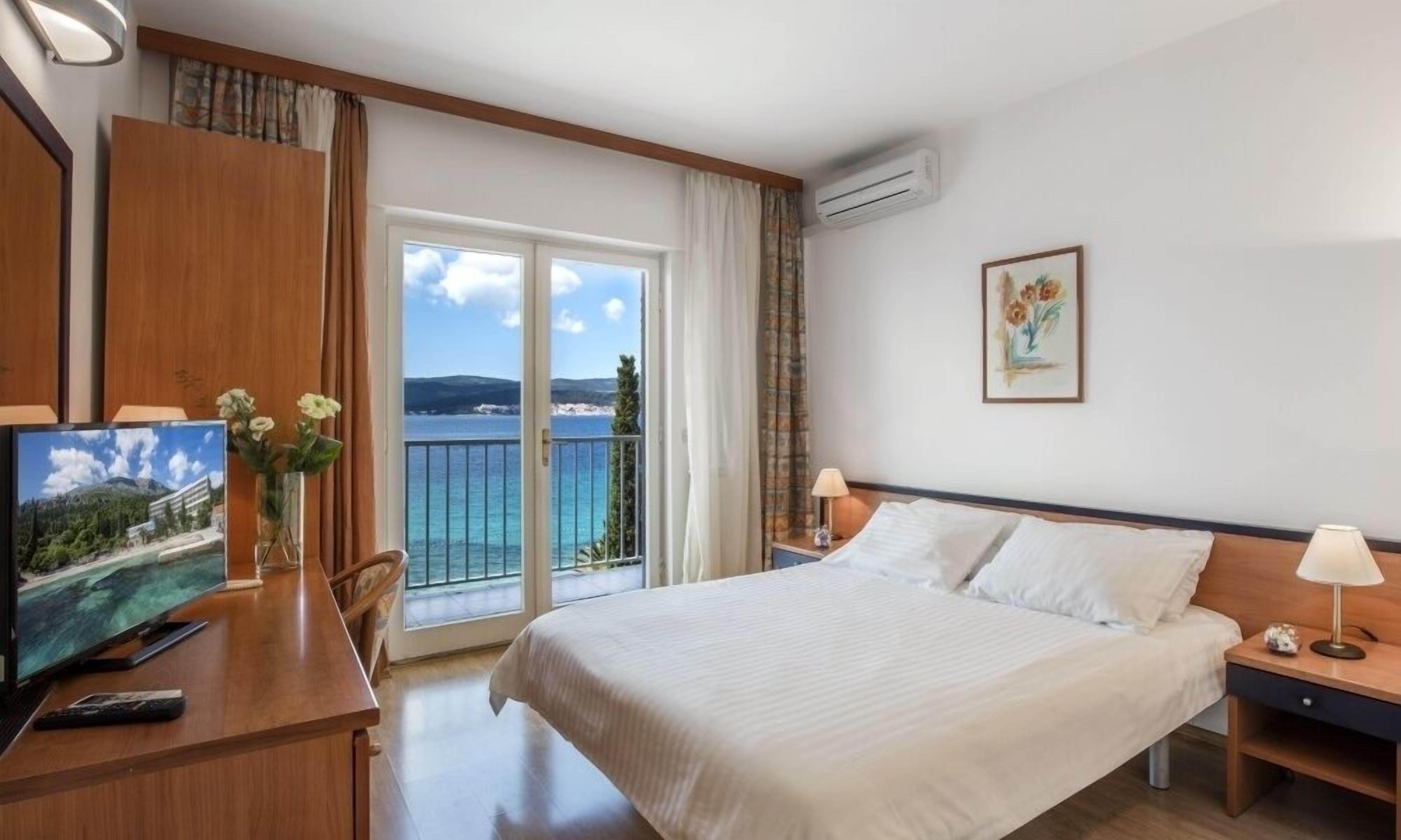 Una camera d'albergo con un letto, una scrivania con televisore, una sedia, un comodino, una lampada e un quadro.