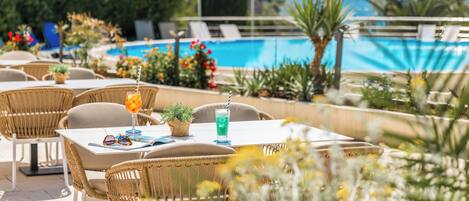 An outdoor seating area with wicker chairs and tables, a pool, and umbrellas.