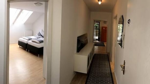 Ein modernes Interieur mit einer Treppe zu einem Schlafzimmer mit Oberlicht, einem Flur mit Fernseher und einer Tür mit goldener Griff.