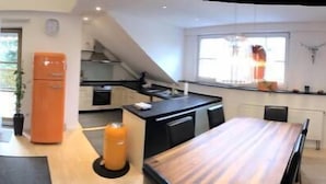 Ein modernes Wohnzimmer mit einer Couch, einem Esstisch und einer Küchenzeile mit einem Kühlschrank.