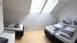 Ein kleiner, gut beleuchteter Raum mit Hochloungebett, einem Einzelbett und einem Schreibtisch.
