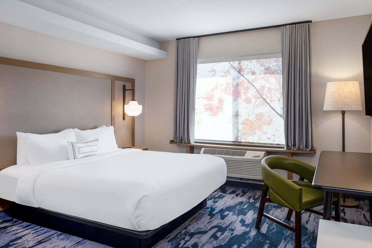 Una habitación de hotel con una cama grande, un escritorio, una silla, una ventana con cortinas y una lámpara.