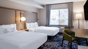 Habitación de hotel con dos camas, un escritorio, una silla, televisión y ventana con cortinas.