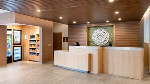 Un área de recepción con un mostrador de madera, una máquina expendedora y un elemento decorativo en la pared.