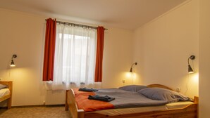 A single wooden bed with a mattress, pillows, and a blanket in a room with a window, a radiator, and wall-mounted lights. - Szigeti Ház, Szécsisziget (Deák Ferenc utca)
