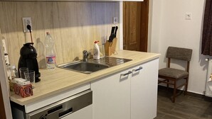 A compact kitchen with white cabinets, a dishwasher, a sink, and a wooden floor. - Szigeti Ház, Szécsisziget (Deák Ferenc utca)
