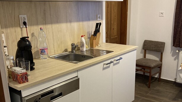 Une cuisine compacte avec des meubles blancs, un lave-vaisselle, un évier et un plancher en bois.