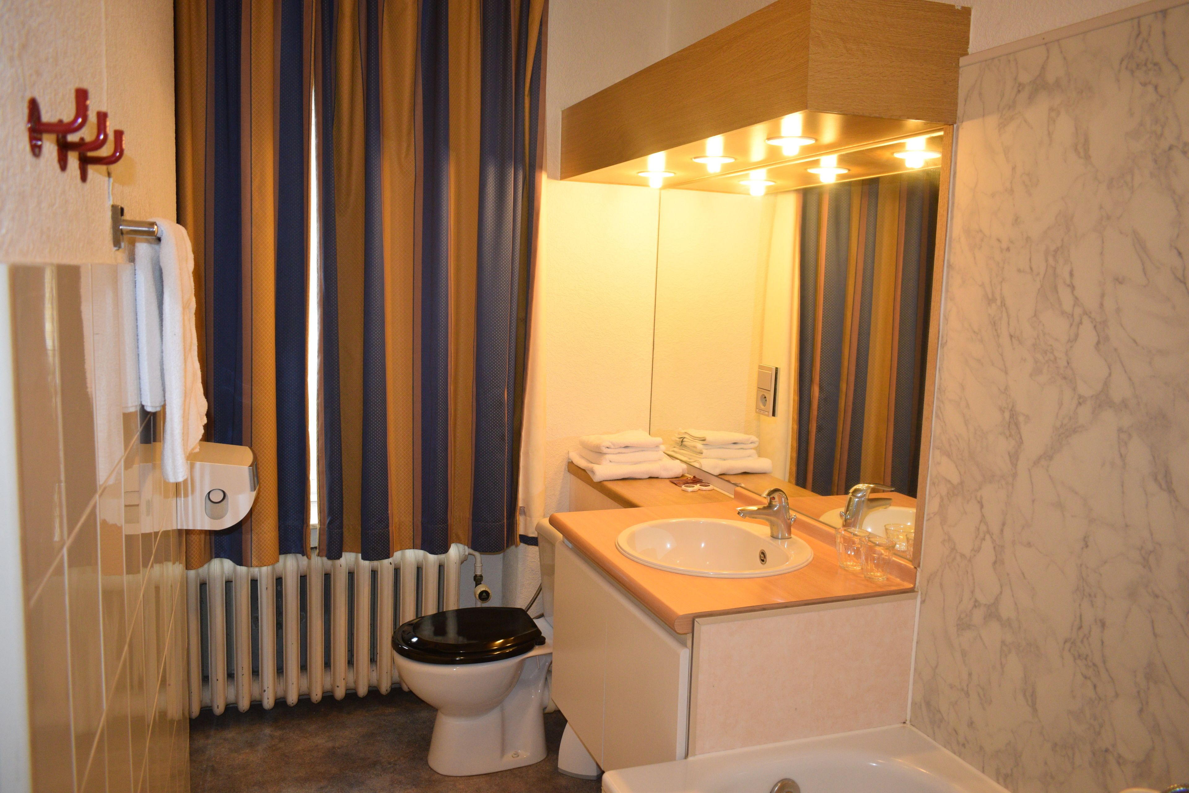A bathroom with a toilet, sink, and mirror. There is a towel rack and a radiator.