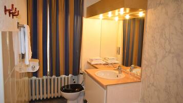 A bathroom with a toilet, sink, and mirror. There is a towel rack and a radiator.