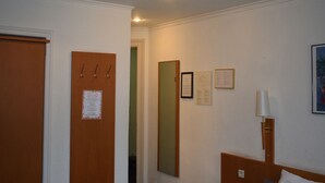 Een hotelkamer met een houten deur, een spiegel, een bed met hoofdeinde en een wandlamp.