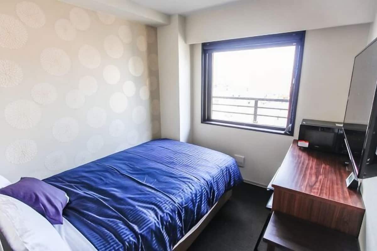 Um quarto com uma cama, escrivaninha, janela e parede estampada.