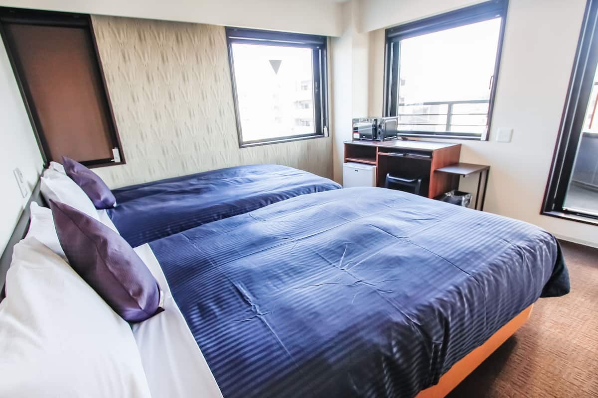 Quarto de hotel com duas camas, uma escrivaninha, uma cadeira e uma janela.
