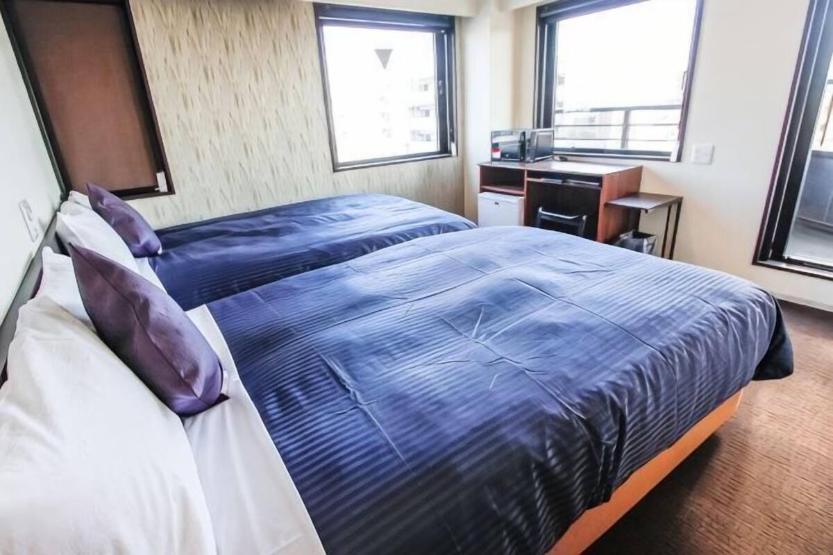 Quarto de hotel com duas camas, uma mesa e uma janela.