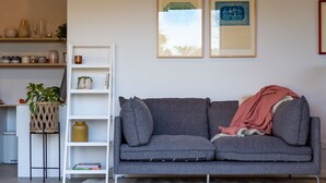 A living room with a grey sofa, a white bookshelf, and two framed pictures on the wall. - Roker Street Retreat - Contemporary Kiwi Styled Studio (Christchurch)