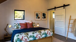 A bedroom with a bed, a nightstand, a lamp, and a door with a ladder. - Roker Street Retreat - Contemporary Kiwi Styled Studio (Christchurch)