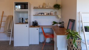 A compact kitchen with a microwave, toaster, and coffee maker. There are shelves with jars and a hanging plant. - Roker Street Retreat - Contemporary Kiwi Styled Studio (Christchurch)
