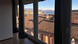 A room with large windows overlooking a cityscape with terracotta rooftops and a body of water. - Angelina's house (Salò)