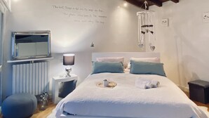 A cozy bedroom with a wooden ceiling, a bed with white bedding, a bedside table with a lamp, and a wall-mounted TV. - Angelina's house (Salò)