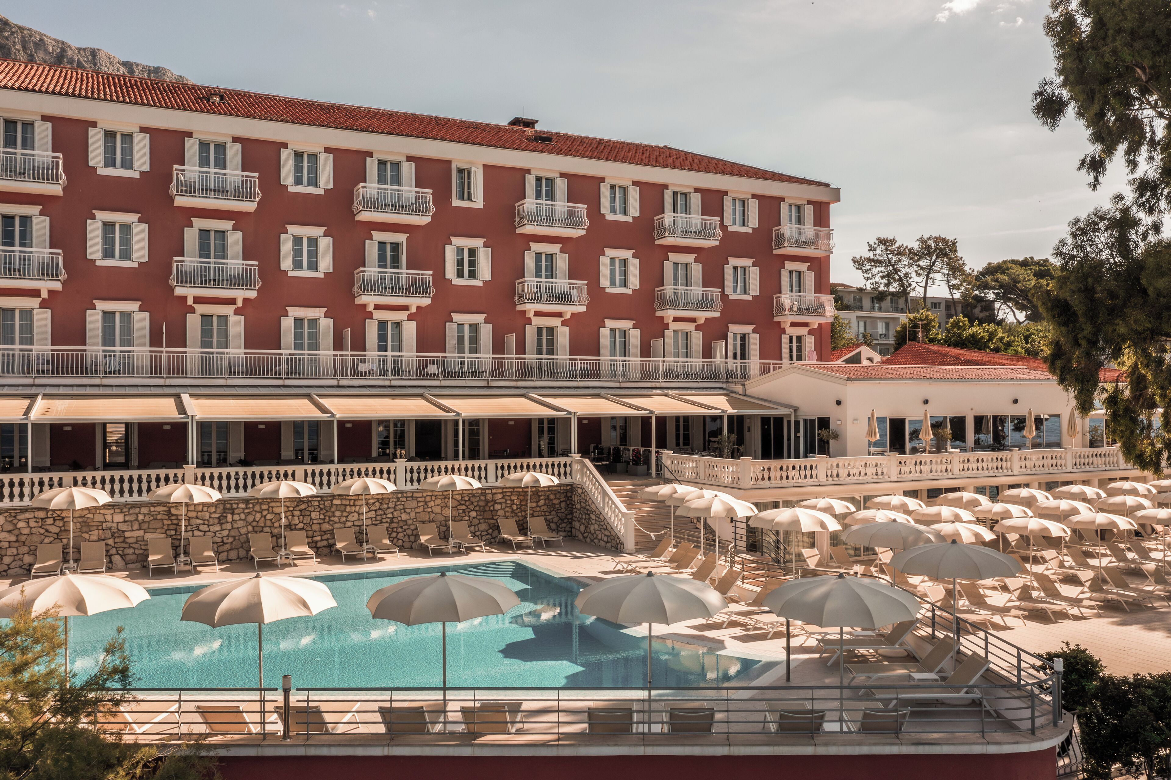 A hotel with a swimming pool, sun loungers, and umbrellas.
