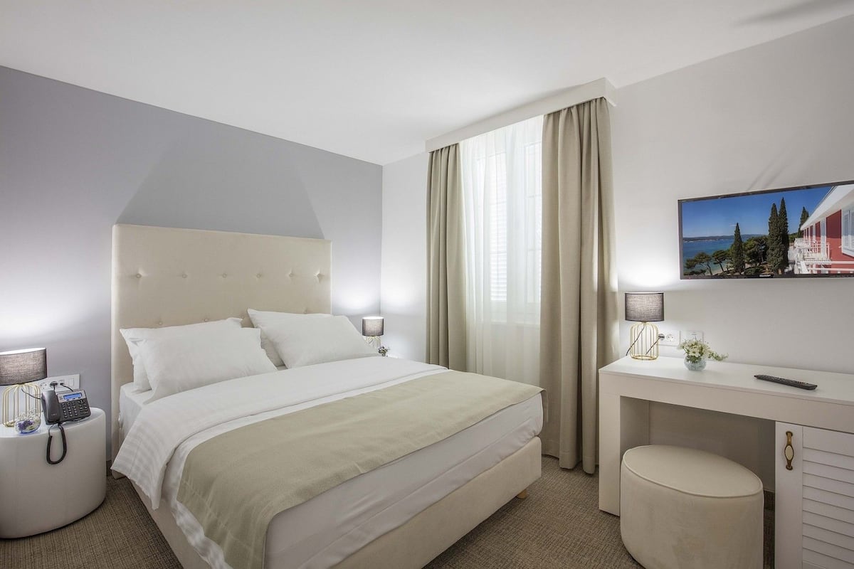 A hotel room with a large bed, a desk with a chair, a telephone, and a painting on the wall.