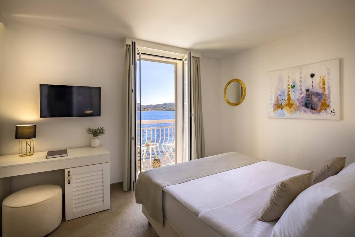 A hotel room with a bed, a desk with a TV, a small table with a plant, and a painting on the wall.
