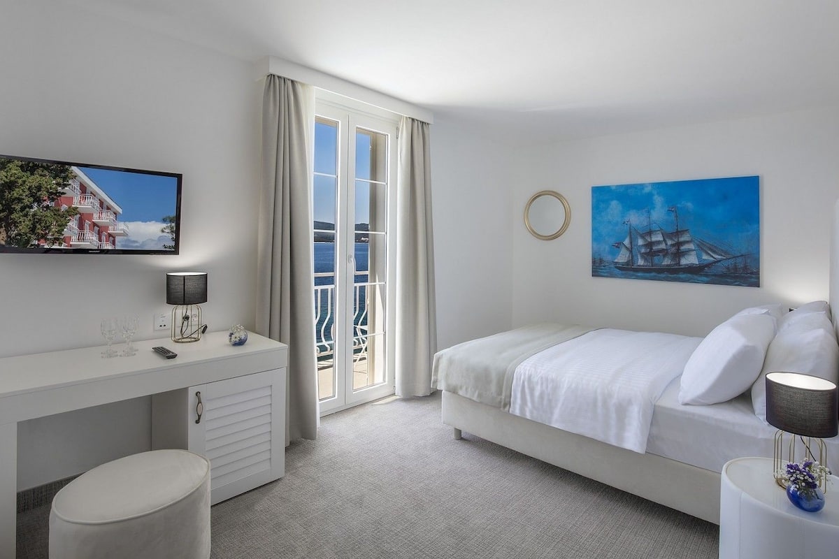 A modern hotel room with a bed, a desk, a TV, and a painting.