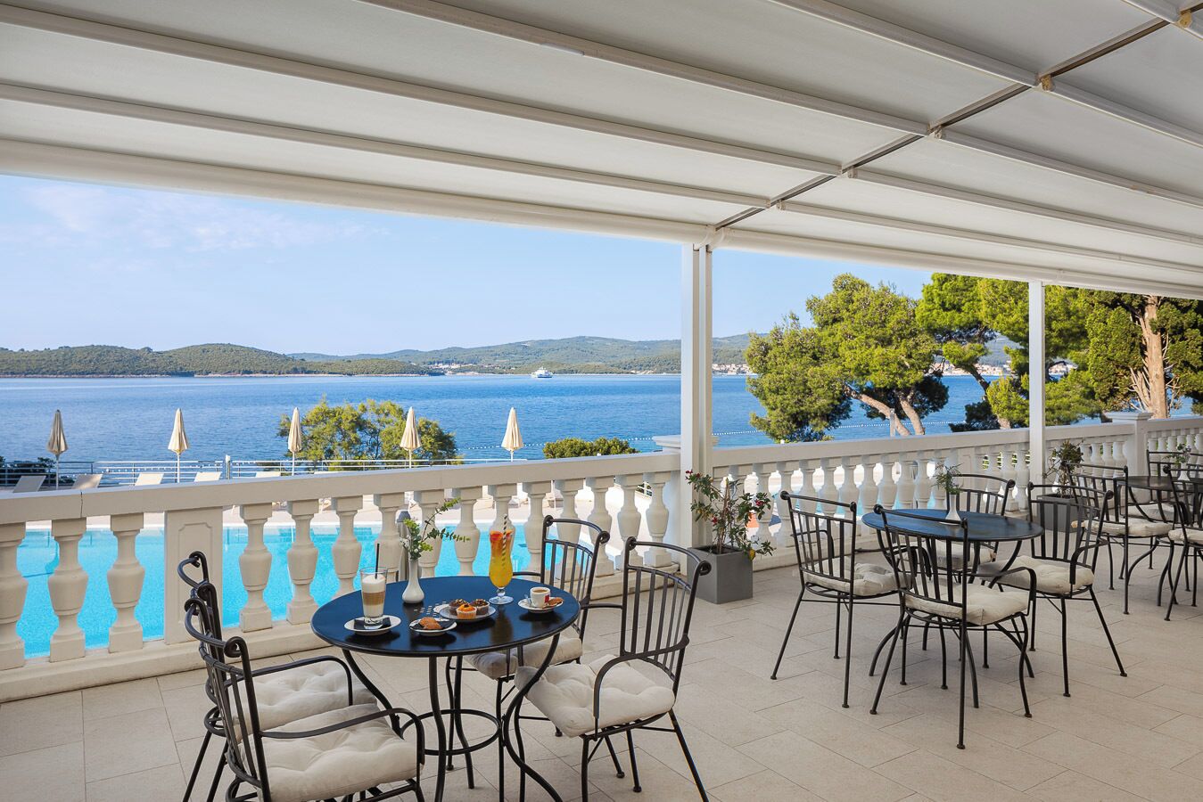 A terrace with outdoor seating, a pool, and a view of the sea and hills.
