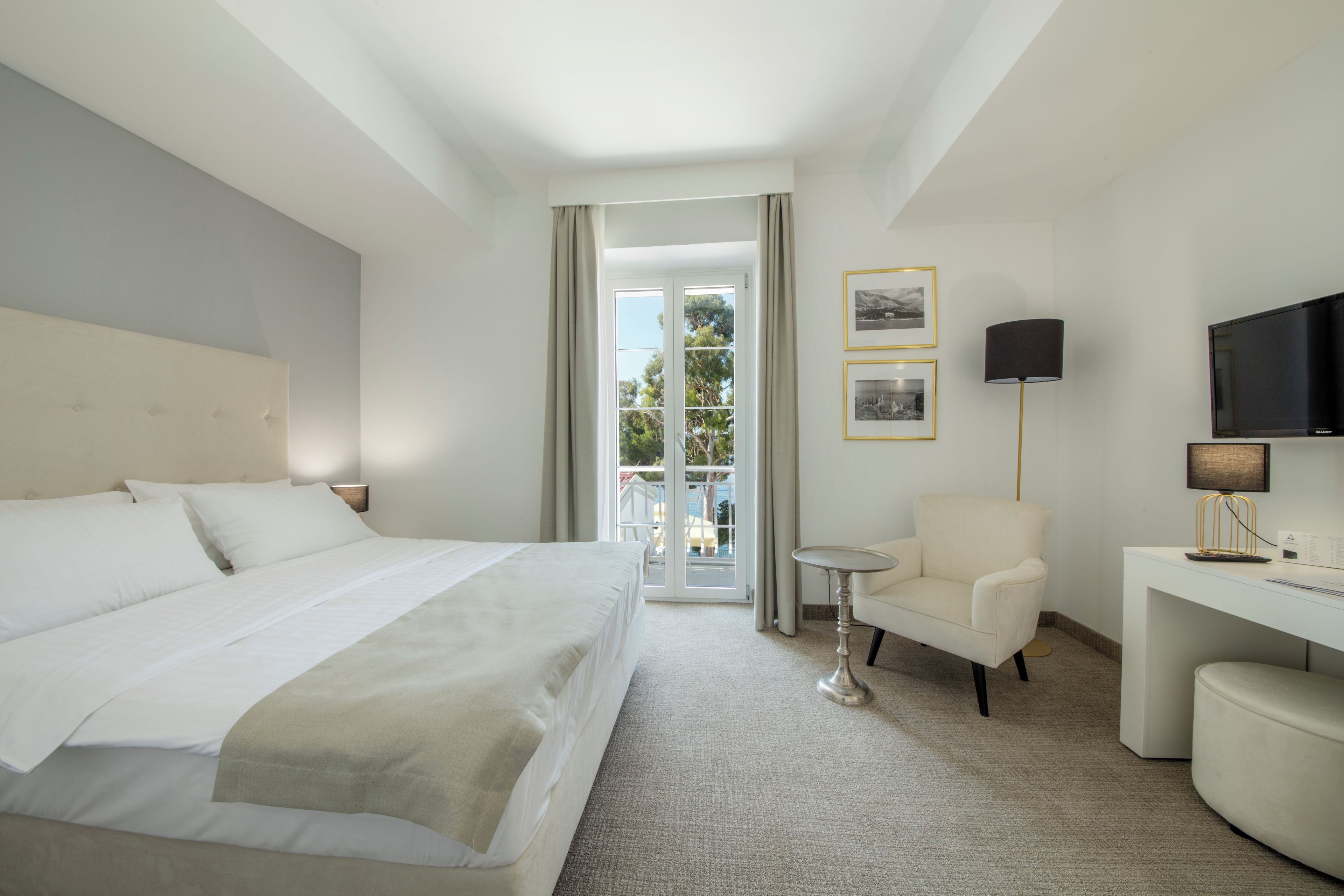 A hotel room with a large bed, a desk, a chair, a TV, and a view of the outdoors.