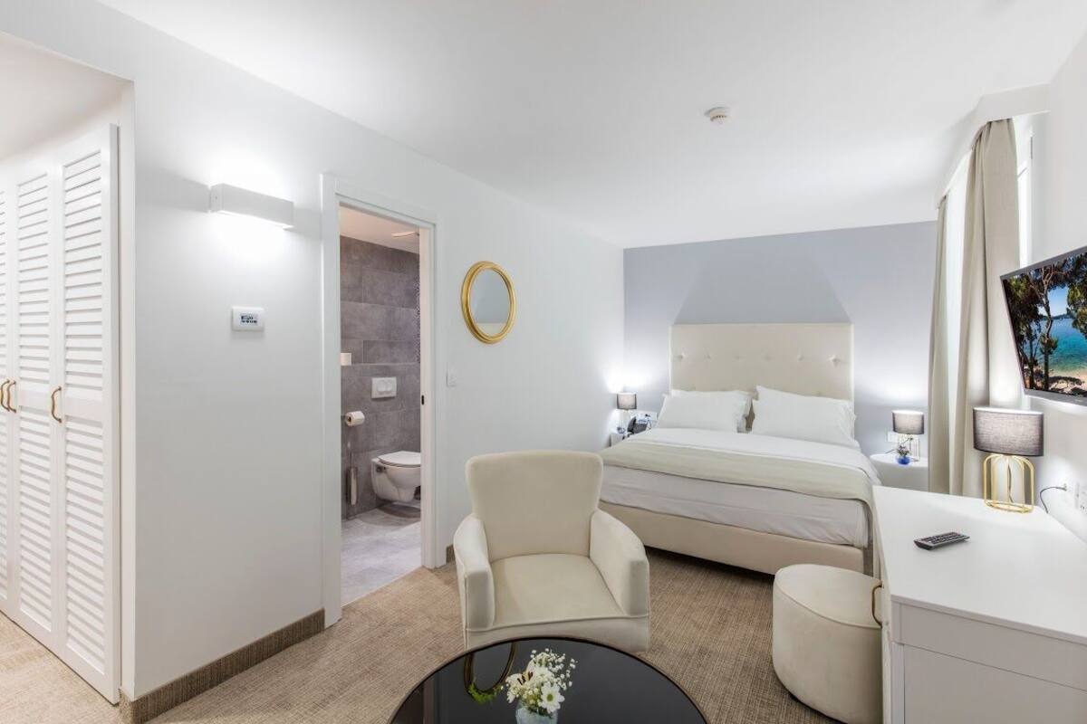 A hotel room with a bed, a chair, a desk, a mirror, and a TV.