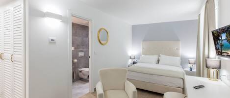 A hotel room with a bed, a chair, a desk, a mirror, and a TV.