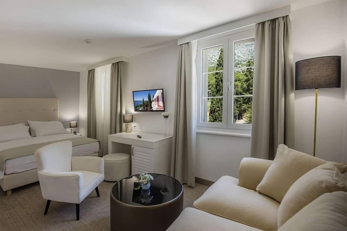 A hotel room with a bed, a desk, a chair, a sofa, a TV, and a window with curtains.