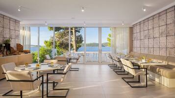 A modern dining area with tables and chairs, large windows with a view of the sea, and a stone wall.