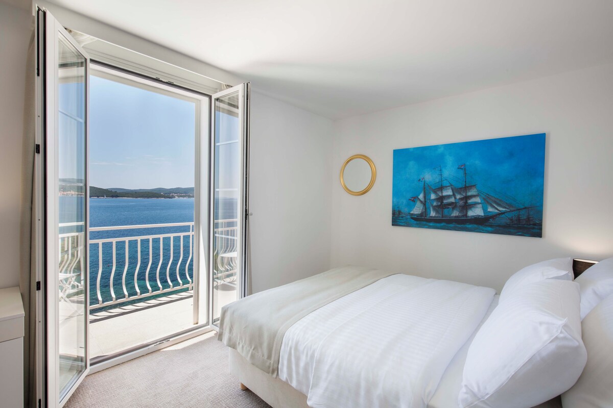 Une chambre à coucher avec un lit, un tableau représentant un navire accroché au mur et une vue sur la mer par une porte coulissante.
