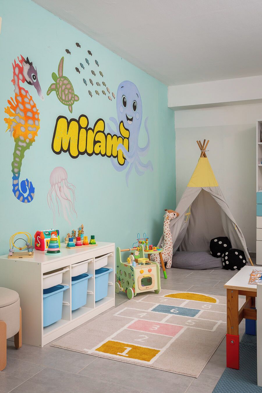 A child's playroom with a wall mural, play area, and storage units.