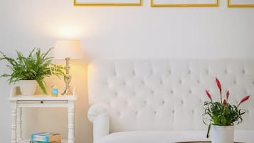 Una habitación con un sofá blanco, una mesa redonda, una mesita auxiliar blanca con una lámpara y tres cuadros en la pared.