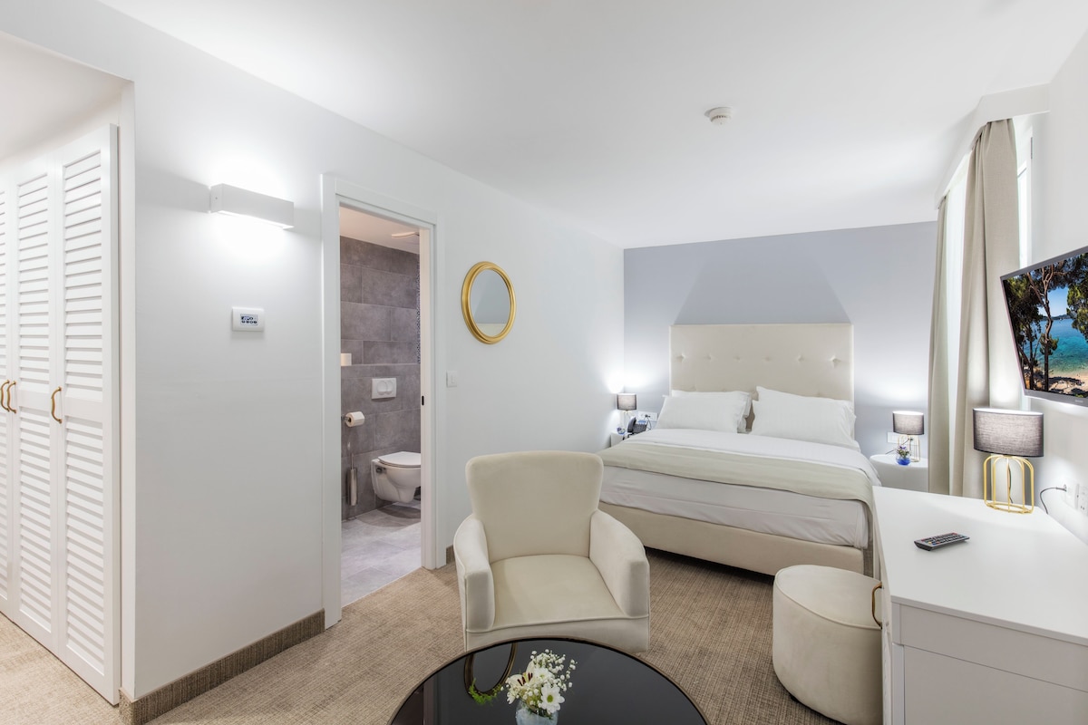 A hotel room with a bed, a chair, a desk, a mirror, and a bathroom visible through an open door.