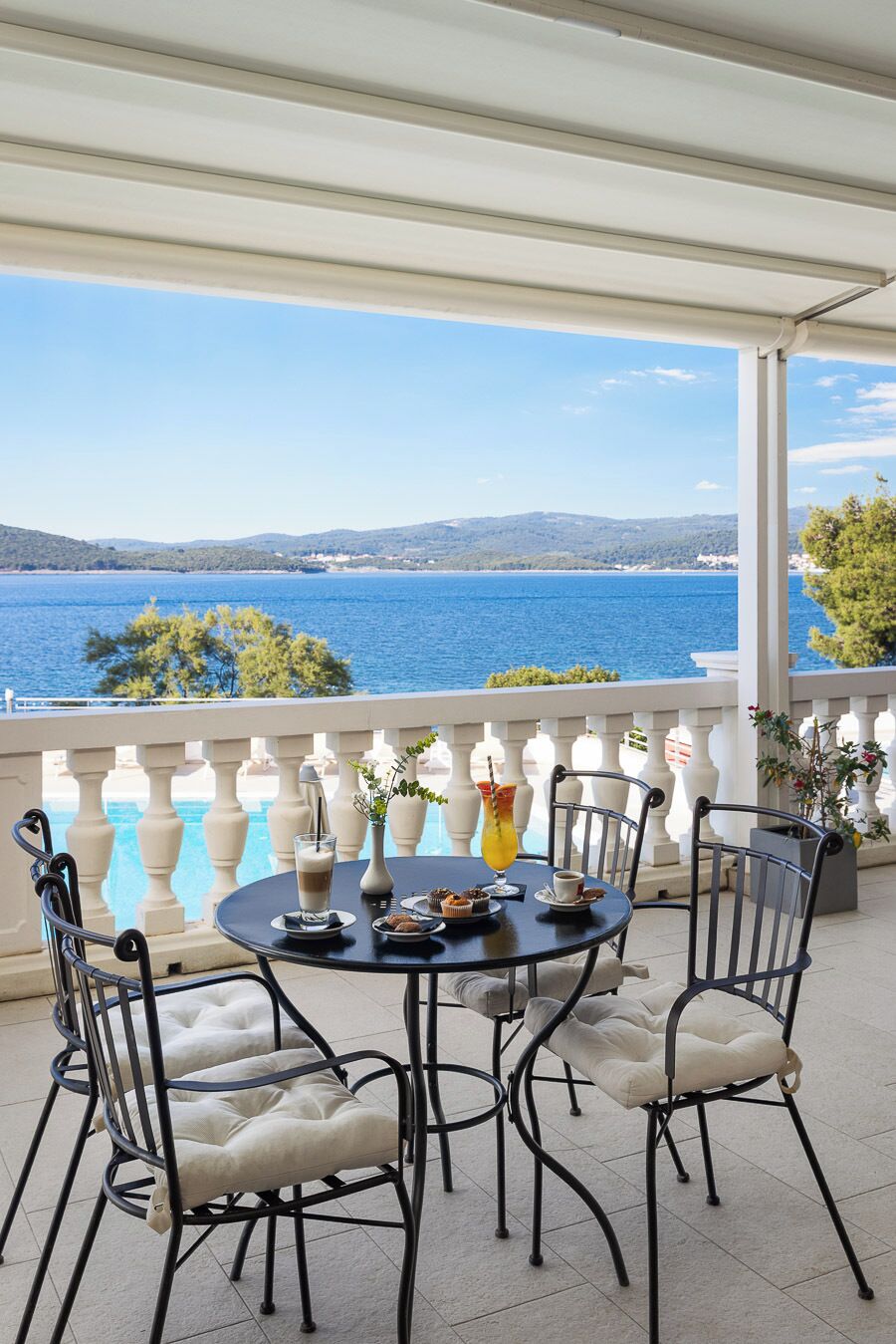 A terrace with a round table and chairs, overlooking a body of water and distant hills.