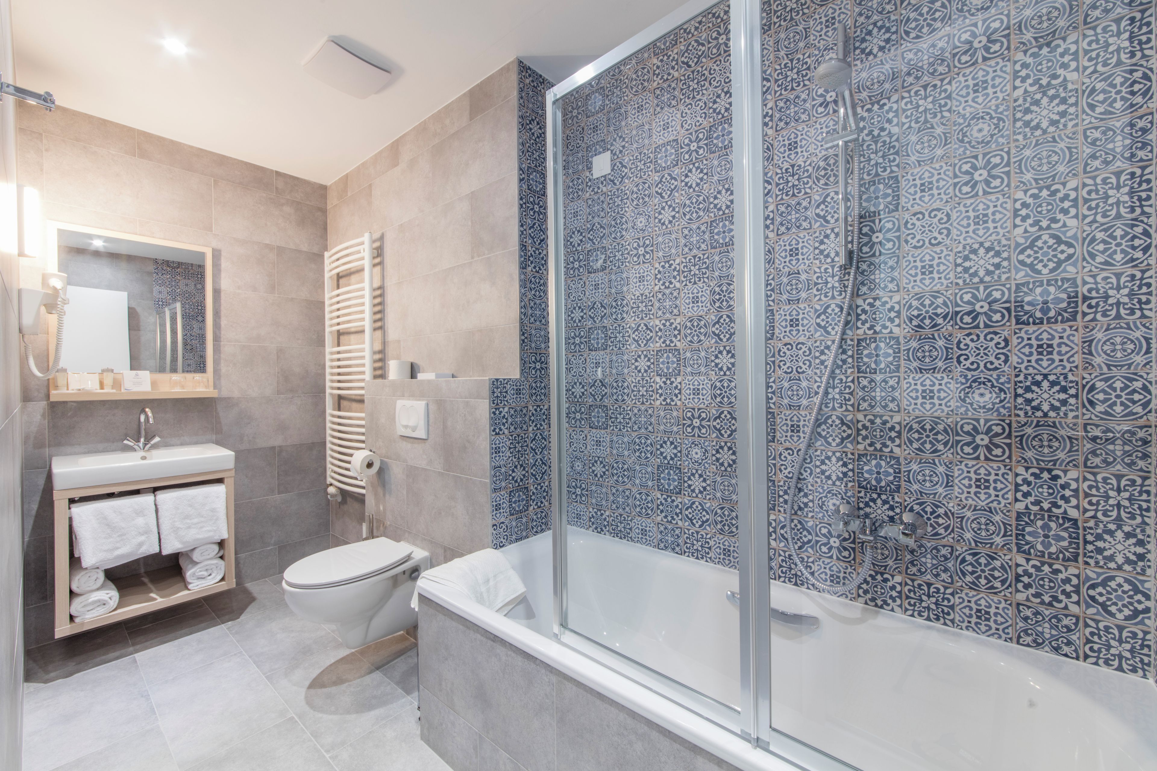 Un baño moderno con ducha de vidrio, inodoro y lavamanos con perchero para toallas.